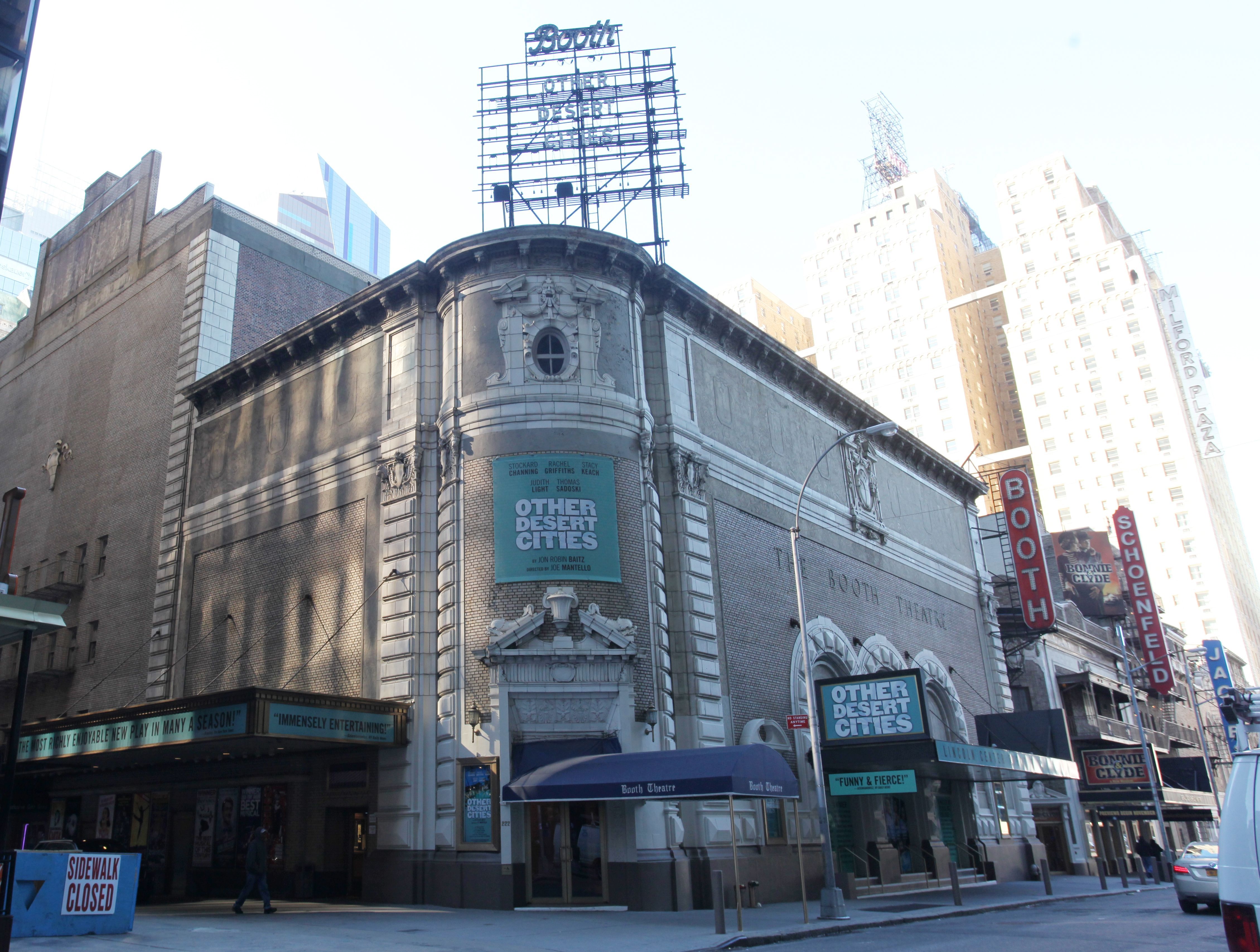 The Booth Theatre, featuring a marquee for "Other Desert Cities," showcases its historic architectural elegance amidst the modern skyline of New York City.