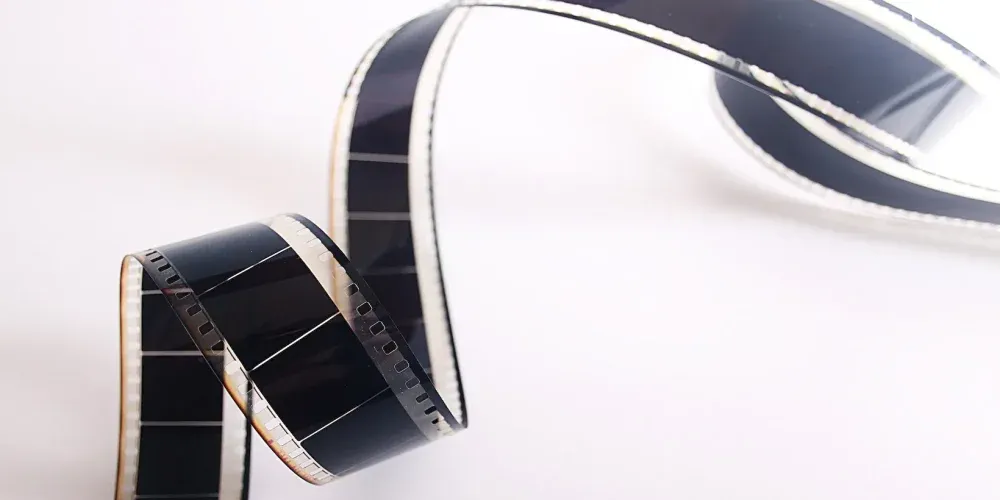 A curled strip of black and white film is coiled artistically, showcasing its perforated edges.