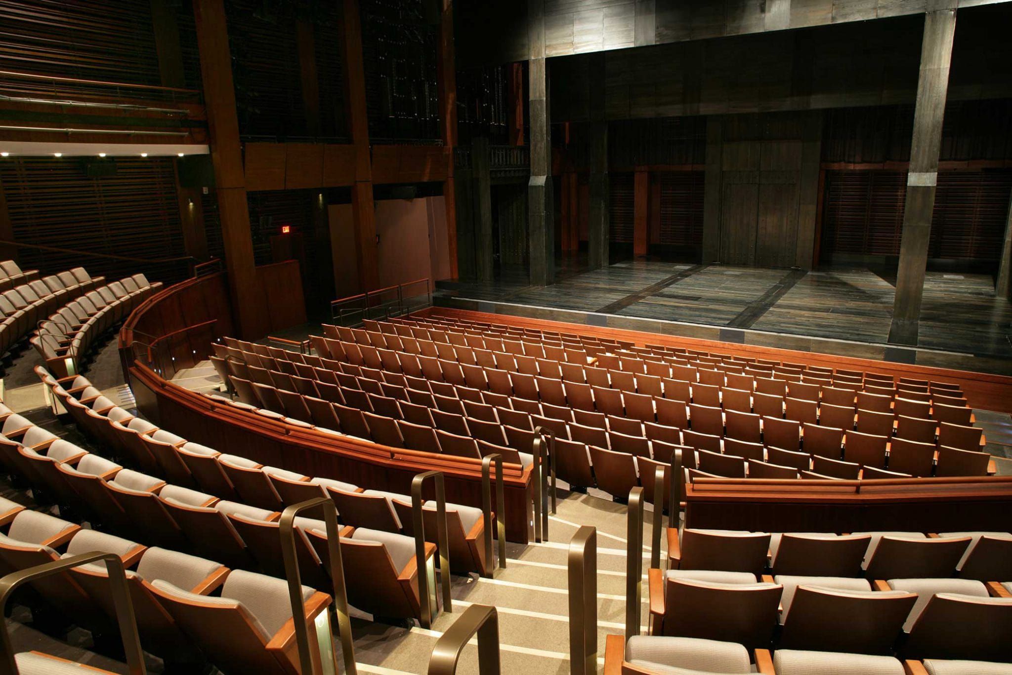 A modern theater features a carefully arranged seating area with plush chairs and a dark wooden stage waiting for a performance.