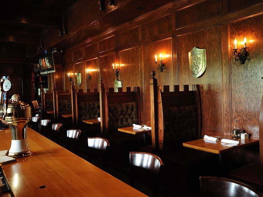 The interior features dark wooden paneling, cozy booths with high backs, soft lighting from wall sconces, and a long bar topped with a polished surface.