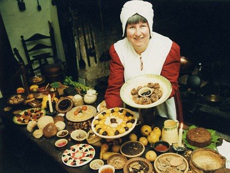 A woman in historical attire presents a lavish spread of various medieval dishes