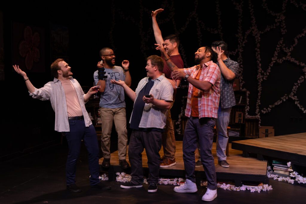 A group of six men joyfully interact on stage