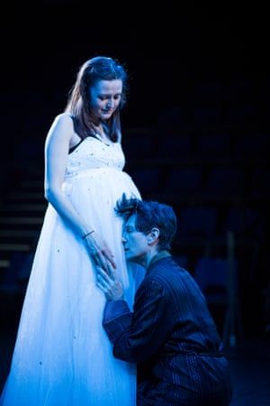 A pregnant woman in a white dress joyfully interacts with a person kneeling before her